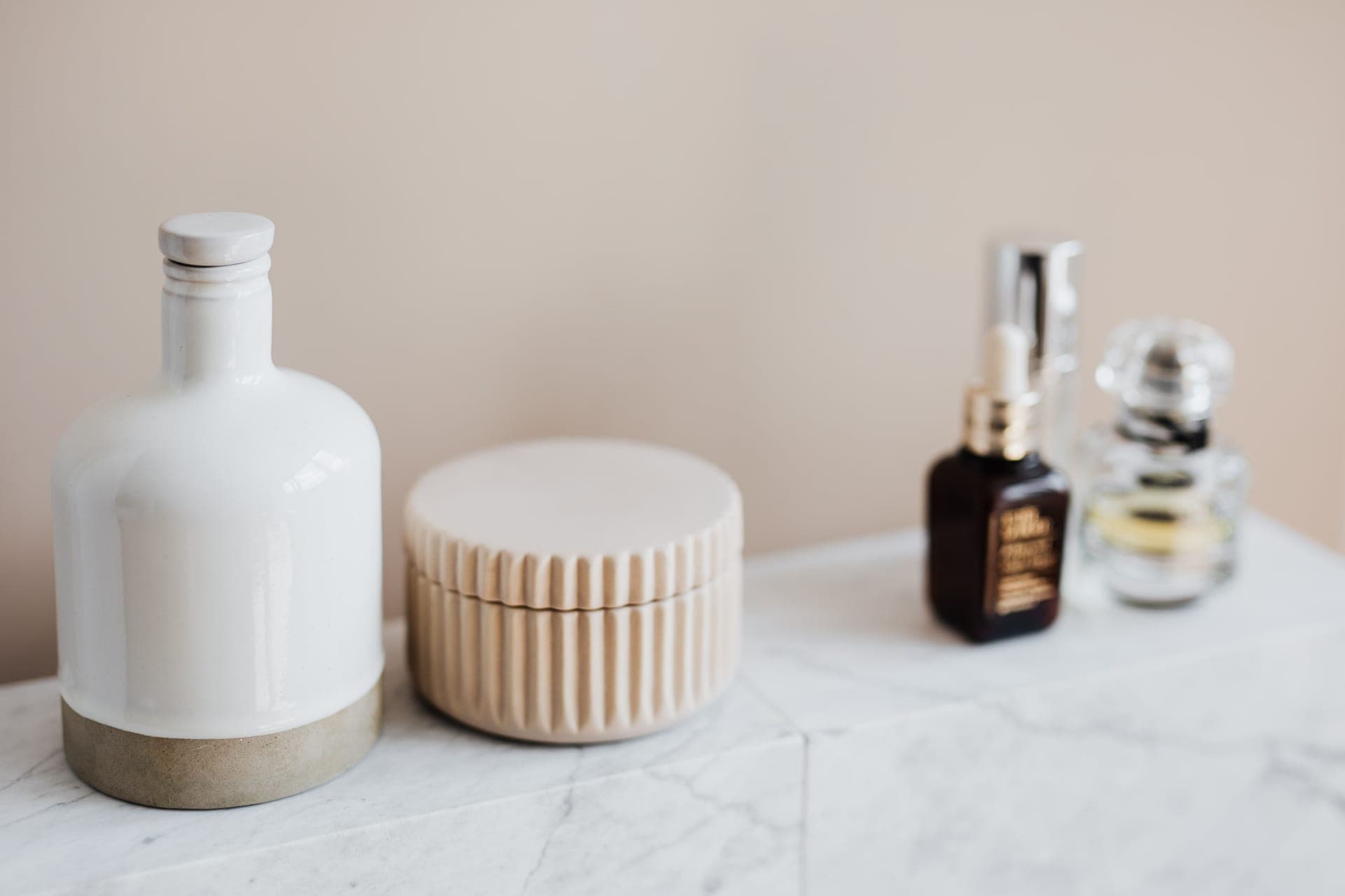 Reusable cosmetic containers and skincare bottles on a white marble shelf in a bright bathroom
