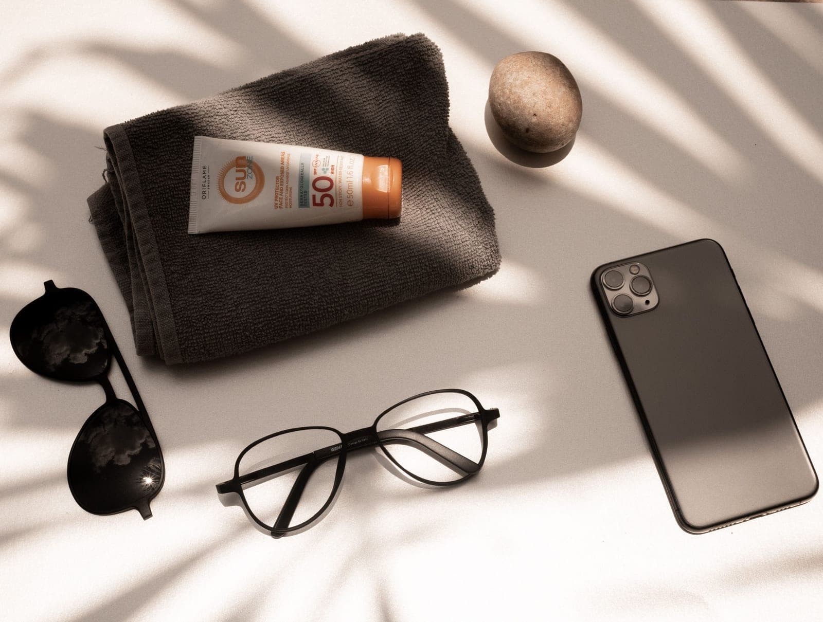 Sunscreen, sunglasses and a towel laid flat in bright sunlight