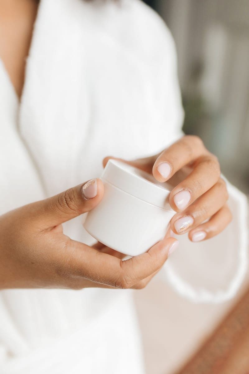 A hand holding a plain white cream container