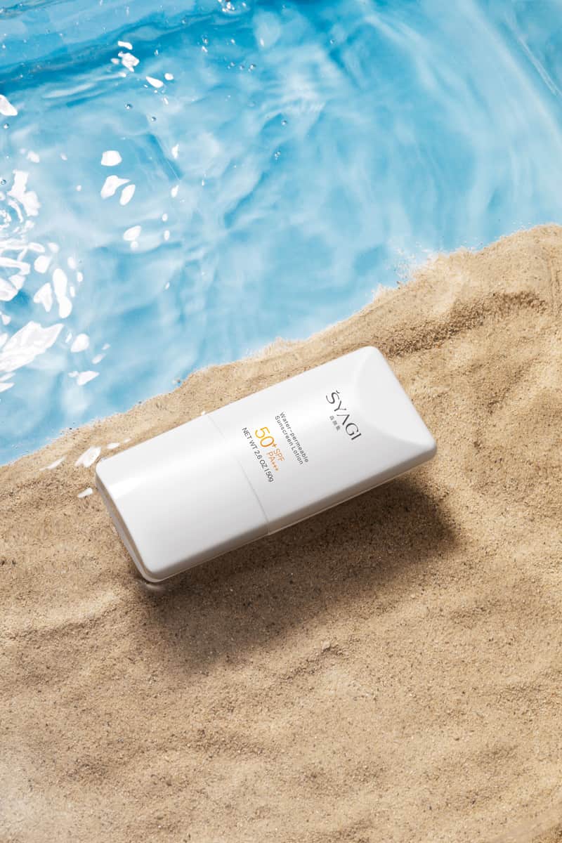 A sunscreen bottle on sand beside clear blue water